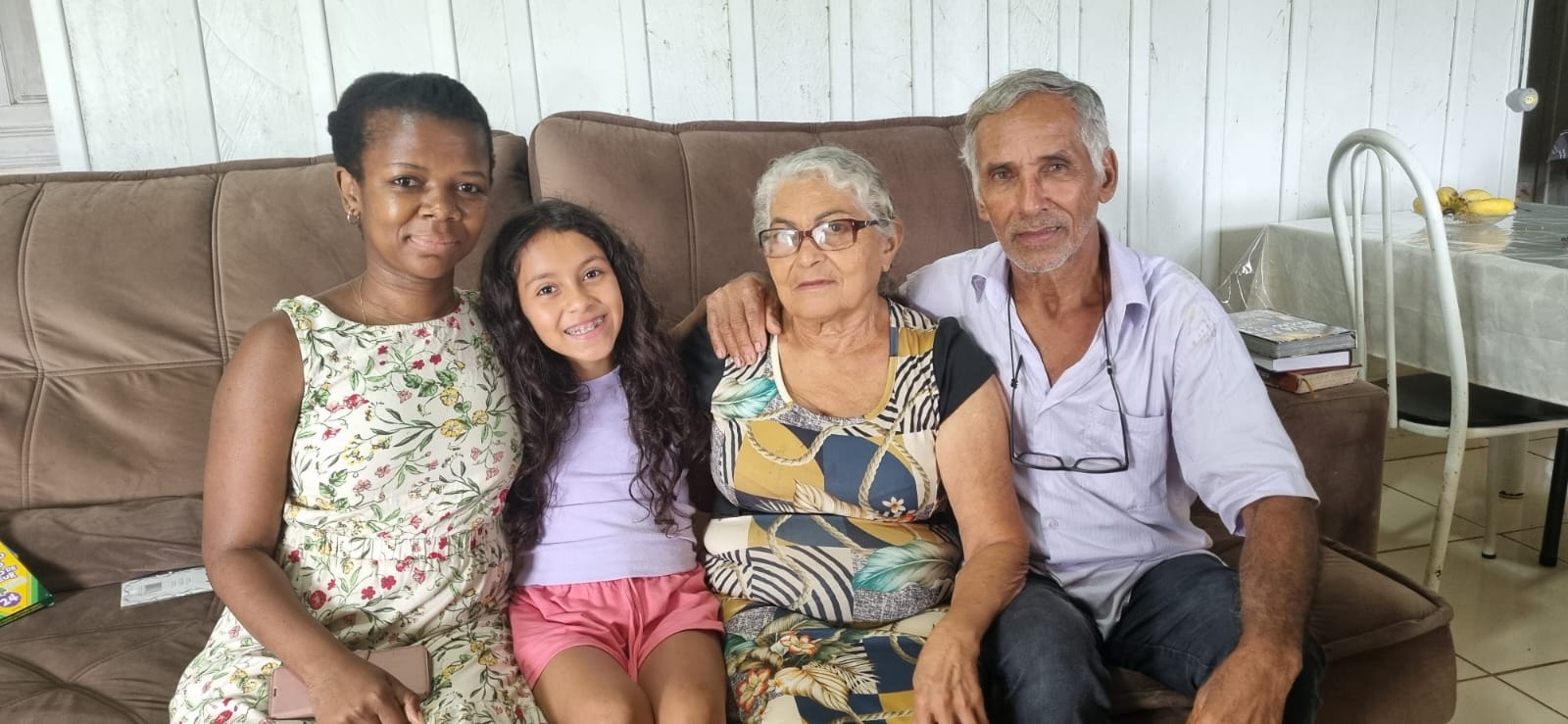 A woman and a man sitting on a couch with two children, smiling together in a cozy living room setting.